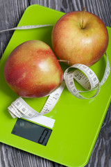 Apples and a measuring tape lie on the scales. Scales show zero. On brushed pine boards. Symbol of World No Diet Day.