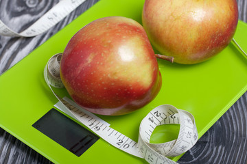 Apples and a measuring tape lie on the scales. Scales show zero. On brushed pine boards. Symbol of World No Diet Day.