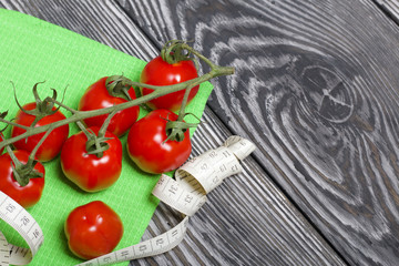 Bunches of tomatoes are on the scales. Near the measuring tape. On brushed pine boards. Symbol of World No Diet Day.