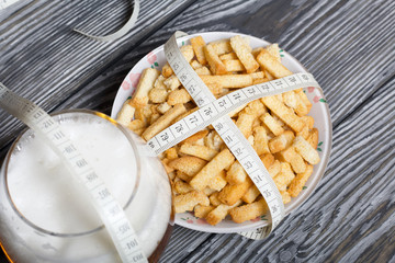 A cup with crackers. Wrapped measuring. Near a glass of beer. On brushed pine boards. Symbol of World No Diet Day.