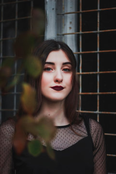 Portrait of a young beautiful girl with dark lipstick near the old window of a green house