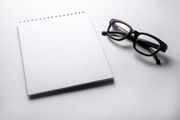 Fototapeta premium White notebook and black glasses on light background