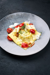 Traditionelle italienische Ravioli Pasta angeboten mit Parmesan Käse und gebratenen Tomaten als closeup auf einem Modern Design Teller