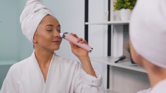 girl in a bathrobe uses a vacuum cleaner for face