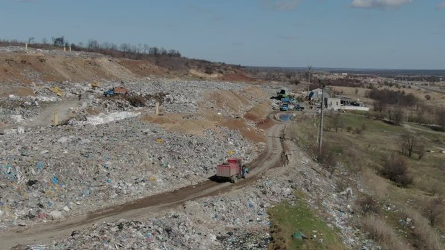 Red truck driving through landfill taking out garbage to city landfill, large amount of plastic, a lot of plastic bags. Lantern poles,small pond, dump truck parking,environmental pollution, top video