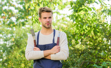 Naklejka na ściany i meble Picnic concept. Bbq chef. Summer weekend. Tools for roasting meat outdoors. Barbeque party. Handsome guy cooking food. Grilling food. Barbecue utensils. Cooking burgers. Man hold barbeque equipment