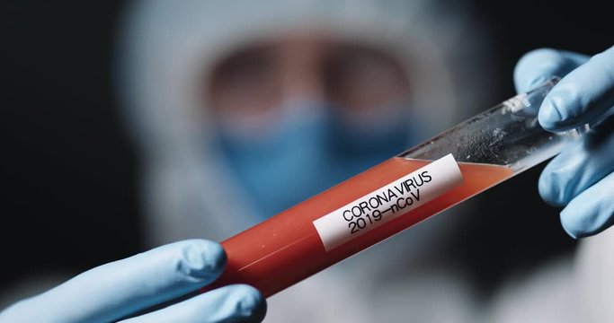 Close up of test tube with vaccine from coronavirus in hands of medic in protected costume. Covid-19 positive test concept. Inventing medicament from virus. Laboratory researching with vaccines.