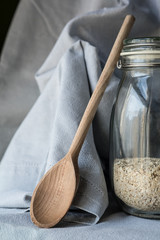 Cristal jar with oat flakes, wooden spoon and blue fabric as background.