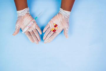 black man's hand wearing gloves holding a syringe with vaccine and some pills