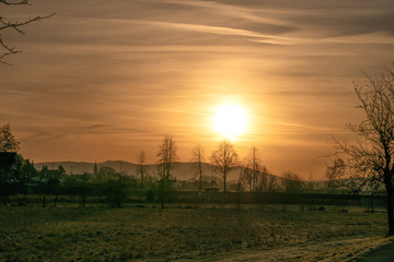 Obraz premium Sunrise on a field with trees and houses in the background