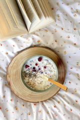 Breakfast bowl and book on a bed. Top view.