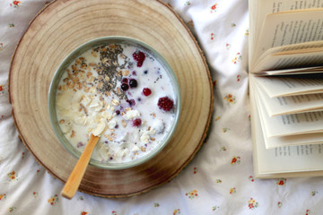 Breakfast bowl and book on a bed. Top view.
