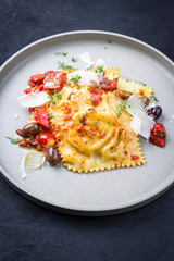 Traditionelle italienische Ravioli Pasta angeboten mit Parmesan Käse, gebratene Tomaten und Oliven als closeup auf einem Modern Design Teller