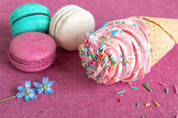 White, blue and purple macaroons, waffle cone with homemade marshmallow and spring flower on a linen napkin. Macarons or macaroons is French or Italian dessert.