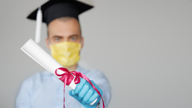 High school graduation during a quarantine. Student graduate in a hat and a protective mask holds a diploma