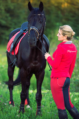 Obraz premium rider women dressed in equestrian wear with black horse posing in green meadow.
