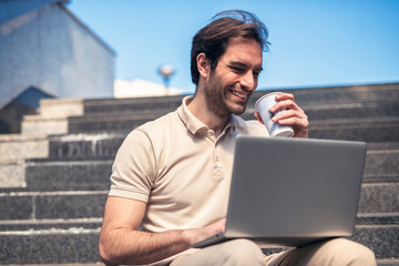 Handsome business man sitting on the steps and working on his laptop, outdoor