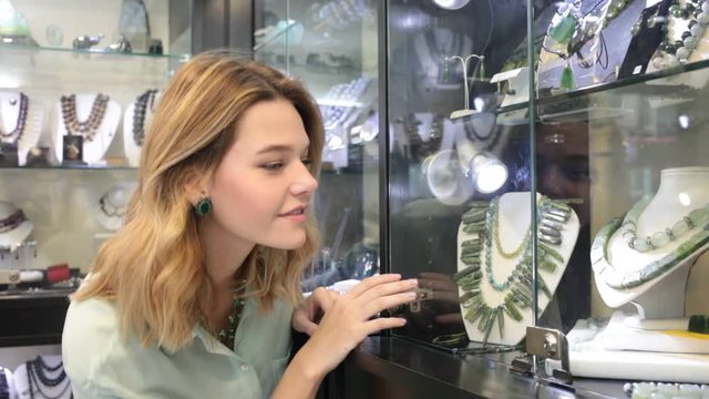 Portrait through glass of young woman choosing necklace in jewelry store