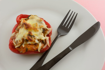 Stuffed red bell pepper with cheese on white plate with black fork and knife