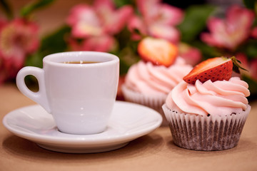 Chocolate cupcakes with strawberries. Cupcakes and a cup of coffee on the table with flowers. Selective focus.