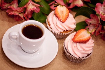 Chocolate cupcakes with strawberries. Cupcakes and a cup of coffee on the table with flowers. Selective focus.