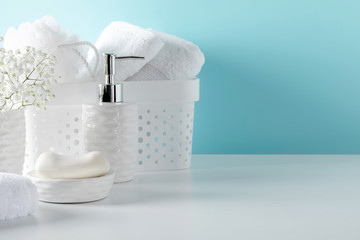 Soft light bathroom decor in pastel blue color, towel, soap dispenser, white flowers, accessories on white wood shelf. Elegant decor bathroom interior.