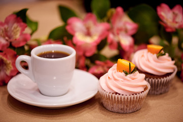 Chocolate cupcakes with kumquat. Cupcakes and a cup of coffee on the table with flowers. Selective focus.