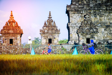 Yogyakarta Indonesia, 4 July 2020 : The boy cycling go to school in the morning from the village, against the background of the Plaosan Temple - obrazy, fototapety, plakaty