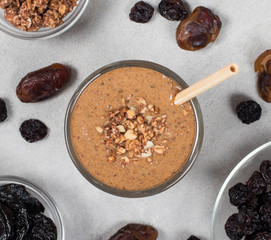 Drink smoothie of dried fruits, prunes, dates, raisins, oatmeal milk with granola and nuts in a glass with bamboo straw on a light background top view