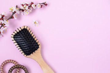 wooden massage comb, spirals for hair and flowering apricot branch on pink background. beauty girl...