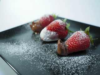 Three strawberries with icing sugar close up