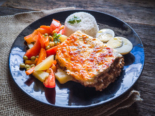 Food dish with Meat hideout with cassava with melted cheese and vegetables. Rustic wood background.