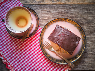 Plate with chocolate covered cake and cup of tea. Rustic wood background.