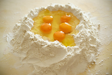 Staying at home with your family and preparing fresh home-made pasta (tagliatelle): flour on a wooden surface with a hole in the middle and eggs inside, volcano shaped.