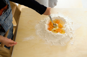 Staying at home with your family and preparing fresh home-made pasta (tagliatelle): the hand of a child mixing flour and eggs to prepare the dough for the pasta.