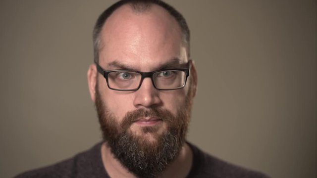 Close up portrait of man with beard and glasses thinking hard or confused about a choice, deep in thought working on a difficult problem to decide.