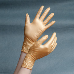 Hands in nitrile gloves of gold color on a gray background with a gradient.