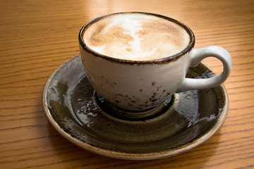 close up of a big cup of cappuccino with art foam design on a yellow wooden table in a cosy cafe