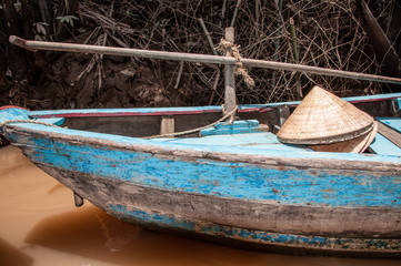 Blue wooden boat with a sun hat sitting on top on the Mekong Delta in Vietnam.