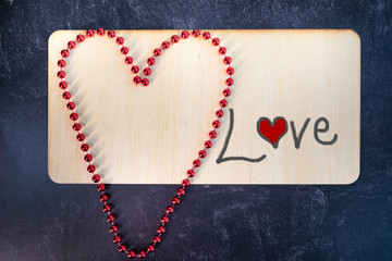 The word Love paint on a wooden sign with a large red hearts shaped out of a red beaded necklace 