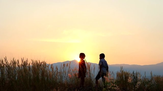 Silhouettes of little boy and girl standing on mountain meadow at sunset