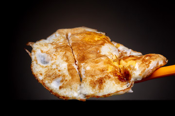 Studio low key still life of a homemade simple fried eggs omelette on a spatula with a half cut through it to divide between people