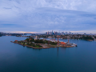 Naklejka na ściany i meble Panoramic drone aerial view over Sydney harbour on a cloudy sunset showing the nice colours of the harbour foreshore