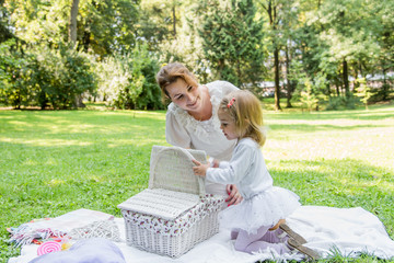 Beautiful little girl in a park on a picnic with straw basket and hat. Spring sunny concept. Happy mothers day. Happy loving family. Mother and daughter.