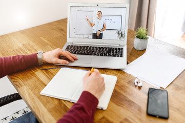 A young woman is online tutor, teacher with flip chart on the laptop screen, male hands write in...