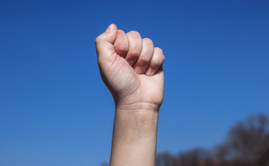 Kid's fist raised up against the clear blue sky, a symbol of fight and resistance movement. Single child's fist raised up showing power, body parts concept, gradient blue sky.	