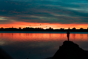 Vibrant sunrise across bay with with silhouette of  figure of person