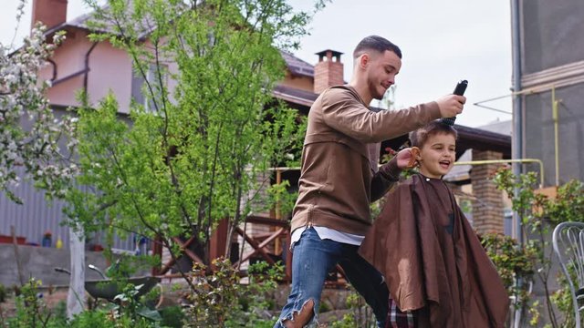 Fun time for a big brother and his small brother make a hair cut in the garden with a electronic clipper in front of the camera