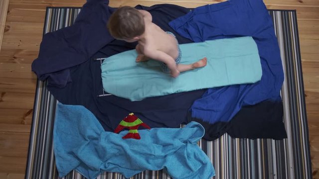 Funny little boy imitating sufring on ironing board at home while isolation. Family activity at quarantine, lockdown. Dreaming about sea, summer 2020 vacation. 