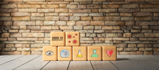 Fototapeta na wymiar cubes with text COVID-19 and health icons in front of a brick wall on a wooden floor